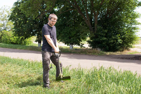 A man with an electric lawn mower mows the grass. For a gardening equipment store with a place for text.の写真素材