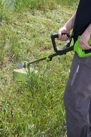 A man with an electric lawn mower mows the grass. For a gardening equipment store, vertical photo.