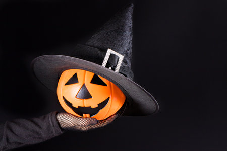 A hand holds a pumpkin lantern jack on a black. Accessories for Halloween. Copy space for textの写真素材