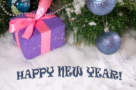 A gift for Christmas in the snow under the tree with text Happy New Year.