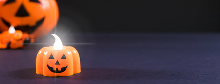 Halloween banner place for text - a candle in the form of a pumpkin glows against a dark background....
