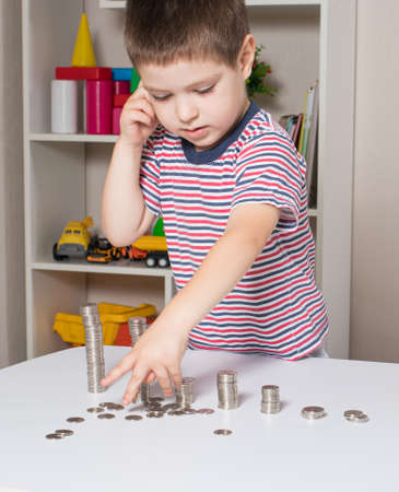 The child is a young businessman learning financial literacy and counting coins. Vertical card.の写真素材