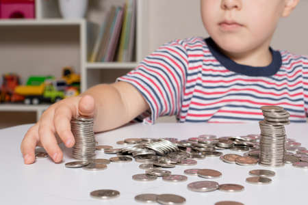 A child in glasses, a young businessman plays with coins and saves money.の写真素材