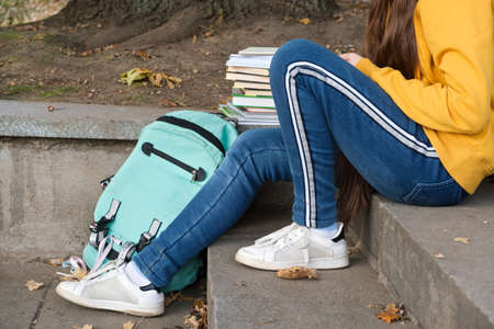 The legs of a teenager sitting on the stairs with books and a backpack.の写真素材