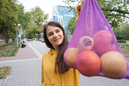 The woman shows a purple transparent fabric bag with fruit.