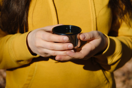 A woman holds a thermo mug of tea in the autumn forest, hands close-upの写真素材