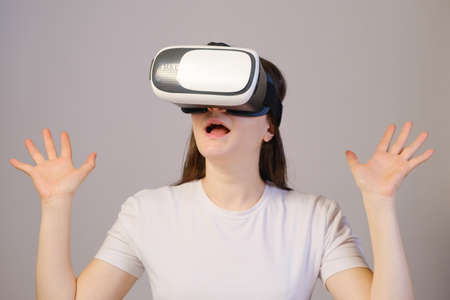A woman in virtual reality glasses with her mouth open raises her hands