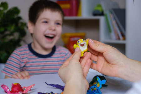 Mother and son sculpt from plasticine of marine animals, yellow funny shark in his hands