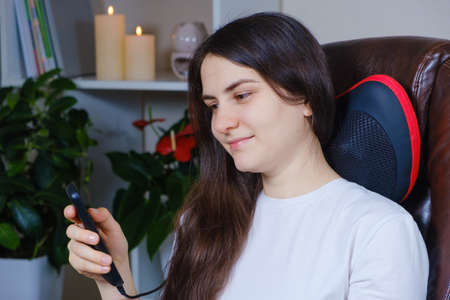 The woman controls the massage pillow under the neck using the control panel.