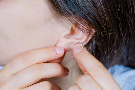 A woman puts on a gold earring in her ear close-up.