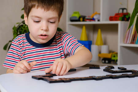 A child in a striped T-shirt plays dominoes. Development and board games for kids.の写真素材