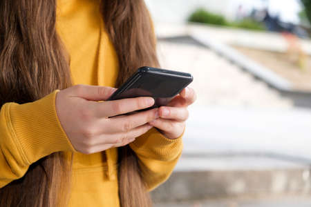 A girl with long hair holds a smartphone close-up.の写真素材