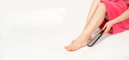 A woman in a pink bathrobe makes a pedicure on a white background, a file for the feet, care for the skin of the heels.の写真素材