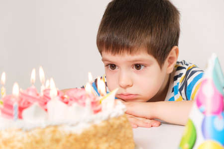 A handsome boy celebrates a birthday, sits in front of a cake with candles and makes a wishの写真素材