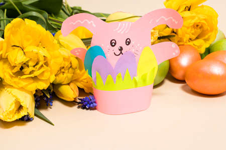 Pink paper Easter bunny and colorful eggs on a beige background, copy space for text.