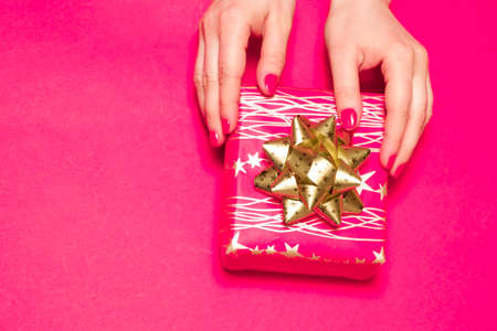 Womens hands holds a gift box on a pink background with space for text.