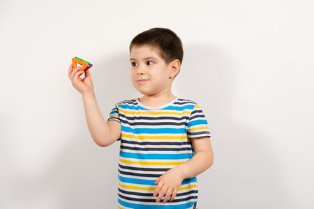 A 4-year-old boy in a striped T-shirt holds the triangles of a magnetic constructor on a white backgroundの写真素材