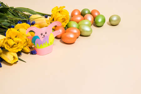 Pink paper Easter bunny and colorful eggs on a beige background with space for text.