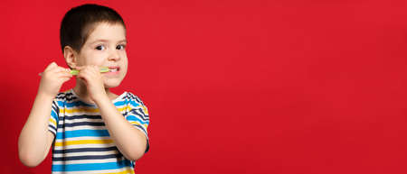 A little boy brushes his teeth with a toothbrush on a red background, banner with place for textの写真素材