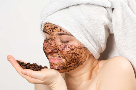 A woman with a coffee mask or scrub on her face holds a handful of coffee beans in her handの写真素材