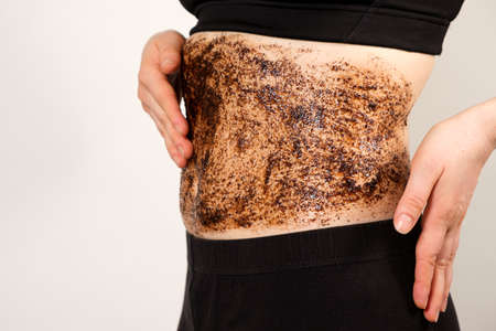 A woman applies a coffee scrub to the abdomen, anti-cellulite massage and peeling of the skin of the abdomen.の写真素材