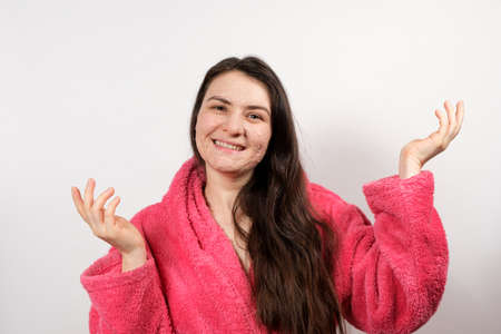 A young brunette woman in a pink bathrobe makes cleansing facial treatments - a mask or scrub to cleanse and nourish the skin.の写真素材