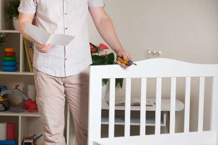The furniture assembler assembles a childrens white wooden bed, studies the assembly instructions