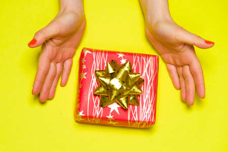 Beautiful red gift box with bow in womens hands on a yellow background, top view, copy space for text.の写真素材