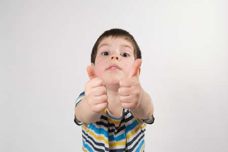 A handsome 4 year old boy points up and looks into the camera on a white background.