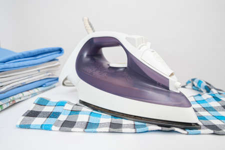 Iron on the ironing board and plaid childrens shirt on a white background. Care of childrens clothingの写真素材