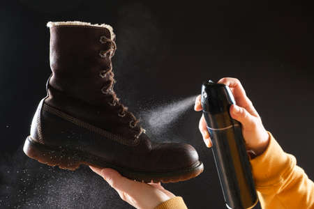 A woman applies the spray to brown nubuck womens winter boots. Water-repellent care for shoes,...