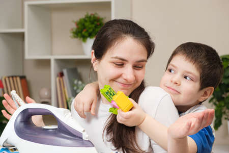 Mother and 4 years old son together iron clothes on an ironing board, care for clothes.の写真素材