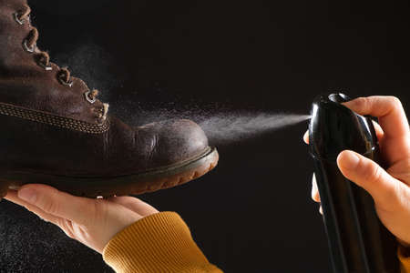 A woman applies the spray to brown nubuck womens winter boots. Water-repellent care for shoes,...