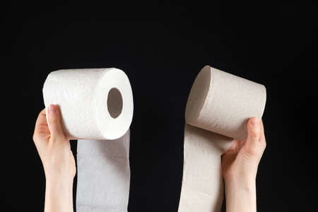 Two types of toilet paper in the hands of a person - white soft paper and gray from waste paper on a black backgroundの写真素材