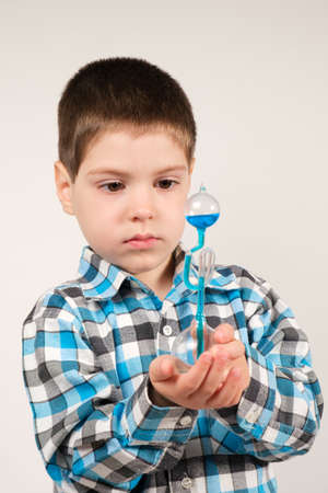 A 4-year-old boy is studying chemistry, holding in his hand a flask with a blue liquid that moves upward from body heatの写真素材