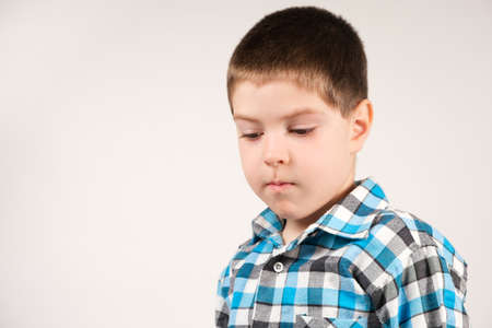 A 4-year-old boy in a plaid blue shirt looks down, squawks or lies, a place for textの写真素材