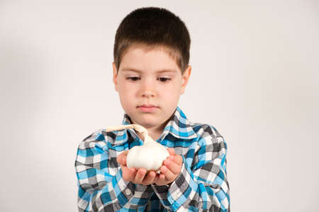 A 4-year-old preschool boy holds garlic on a white background. Vegetables and vitamins for children.の写真素材