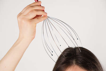 A woman with a metal flexible massager for self-massage of the head on a white background, copy the place for the textの写真素材