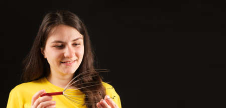 A woman with a metal flexible massager for self-massage of the head on a black background. Banner with place for text.の写真素材