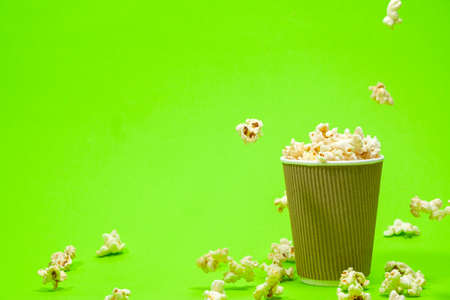 Popcorn is poured into a paper brown glass on a green background with place for text.の写真素材