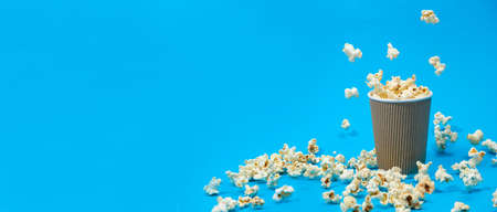 Popcorn is poured into a paper brown glass on a blue background with place for text.の写真素材