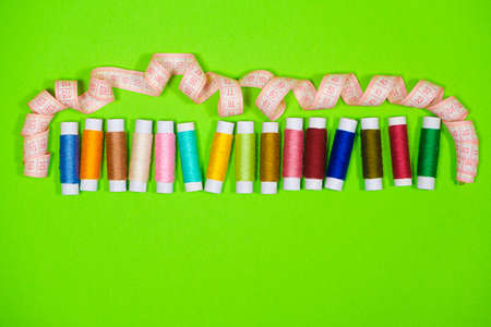 A set of multi-colored threads for sewing and a measuring tape with a space for text on a green...