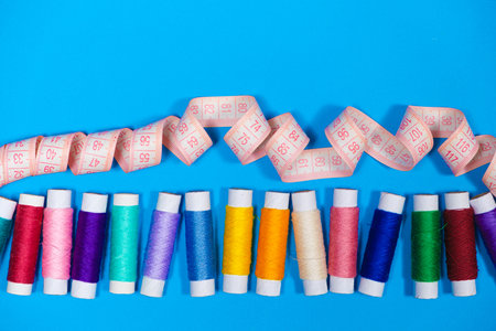 A set of multi-colored threads for sewing and a measuring tape on a blue background, top view....
