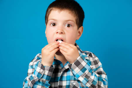 A beautiful preschool boy eats vitamin C or other medicine or dietary supplement on a blue...