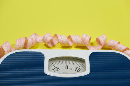 Floor blue scales and centimeter measuring tape on a yellow background, top view. The concept of weight loss and weight controlの写真素材