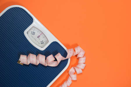 Floor blue scales and centimeter measuring tape on an orange background, top view. The concept of weight loss and weight controlの素材 [FY310187254402]