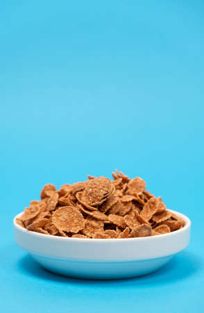 Durum wheat flakes - quick breakfast cereal on a plate on a blue background, space for text