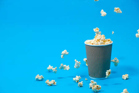 Popcorn is poured into a paper brown glass on a blue background with place for text.の写真素材