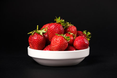 Red fresh strawberries in a white plate on a black background. Summer seasonal berries, close-up