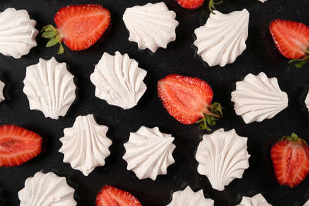 White meringue with strawberries on a black background, top view. Sweet dessert of sugar and egg white with fruitの写真素材